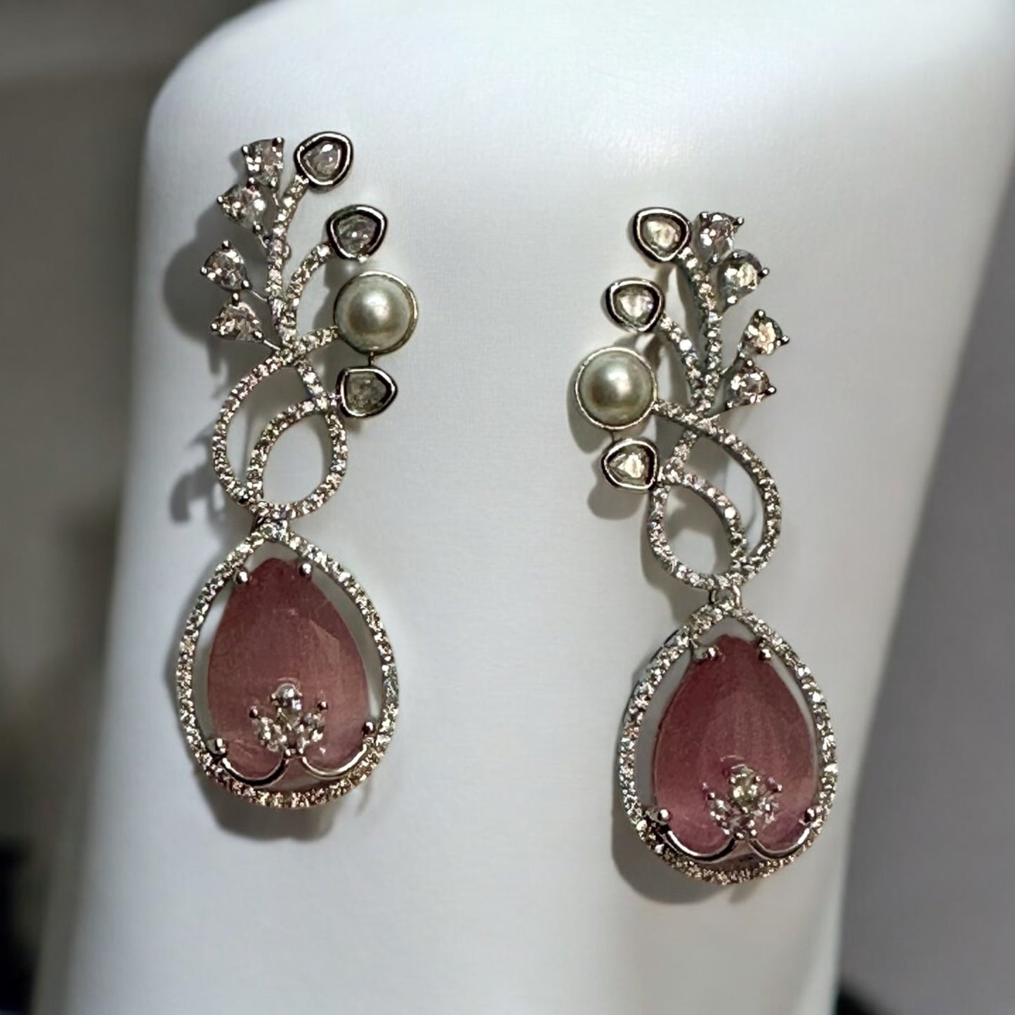 Beautiful American Diamond Statement Earrings In pinkish Shade placed on a white coloured jewellery display stand with a leaves design.