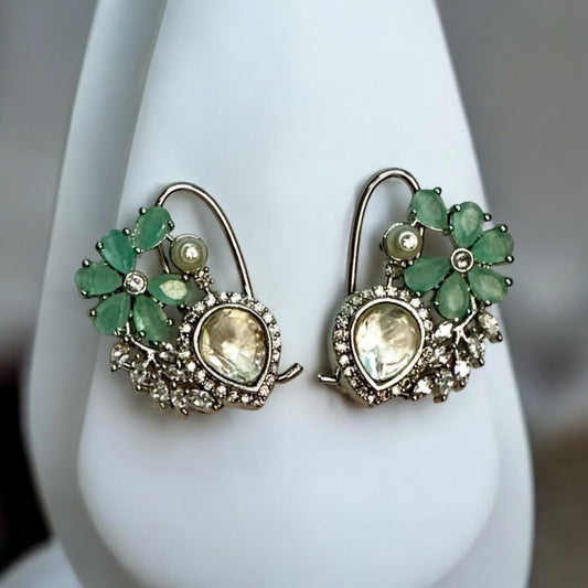 Exquisite American diamond partywear earrings with green floral detailing and pearl accents placed on a white jewellery display stand.