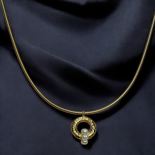 Anti-tarnish gold chain with a circular pendant featuring intricate detailing and three small pearls, displayed on a rich black satin fabric background.