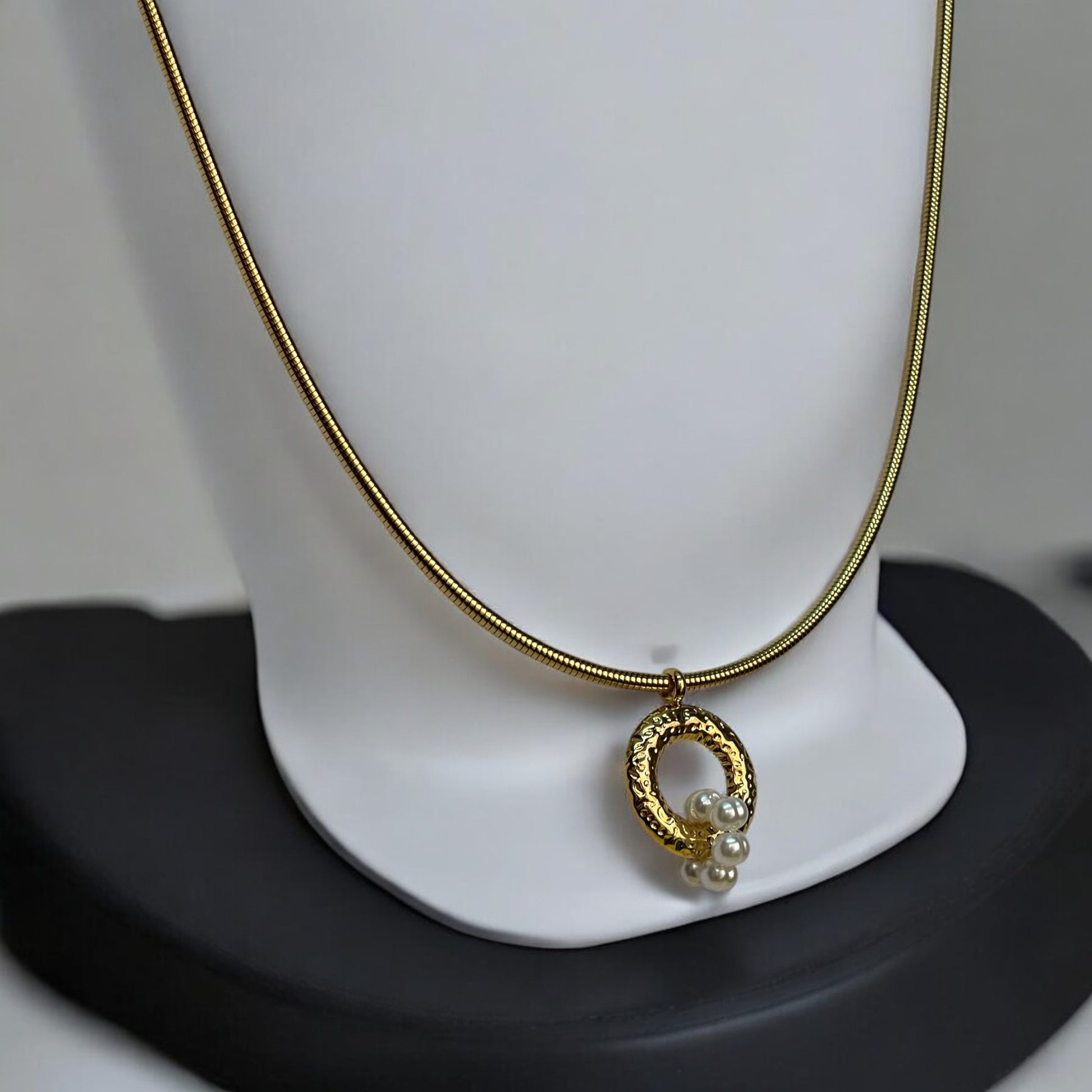 Anti-tarnish gold chain with a circular pendant featuring intricate detailing and three small pearls, displayed on an off white coloured jewellery display stand.