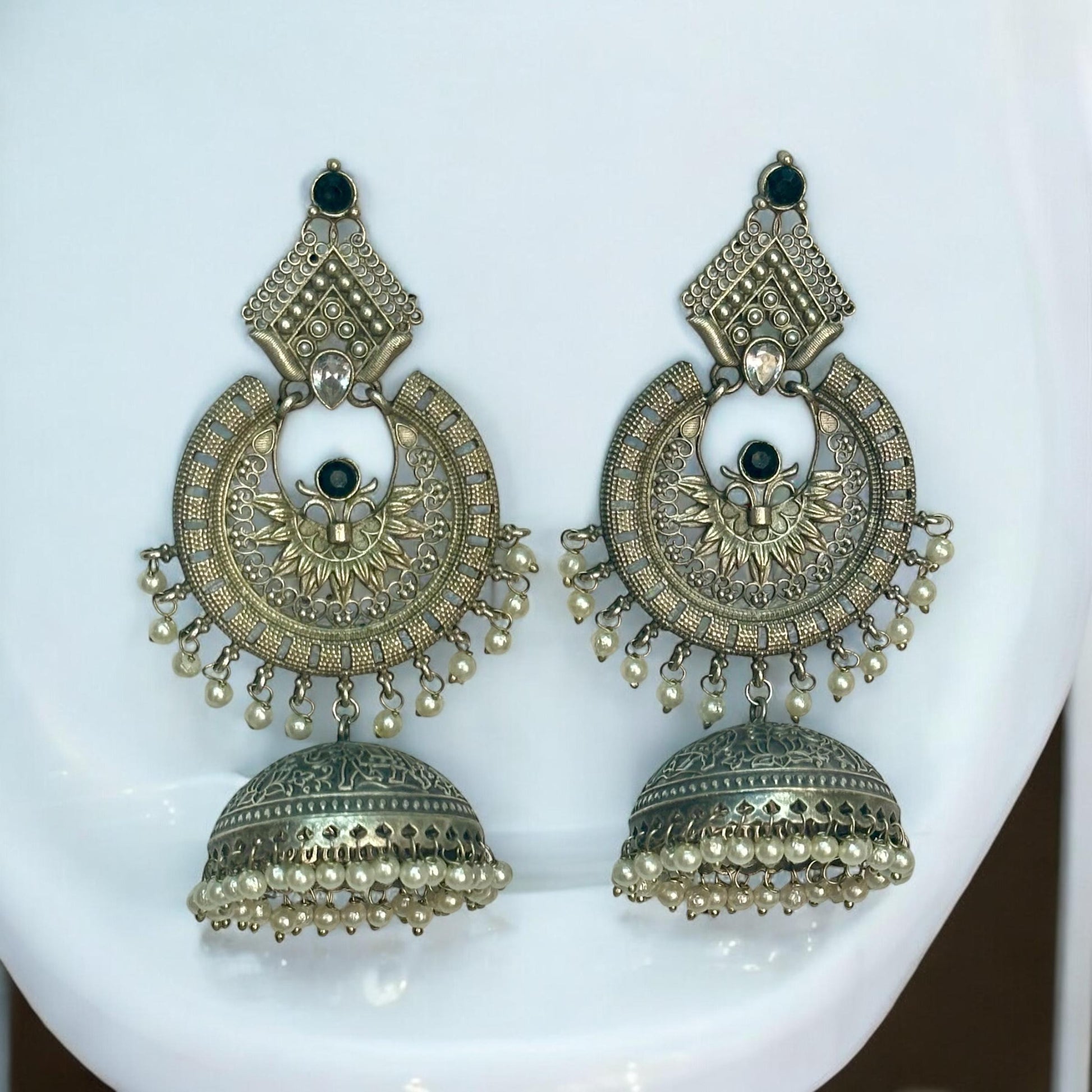 Apala Polish Silver Statement Earrings with Intricate Jhumki Design and Pearl Detailing placed on a white coloured jewellery display stand.