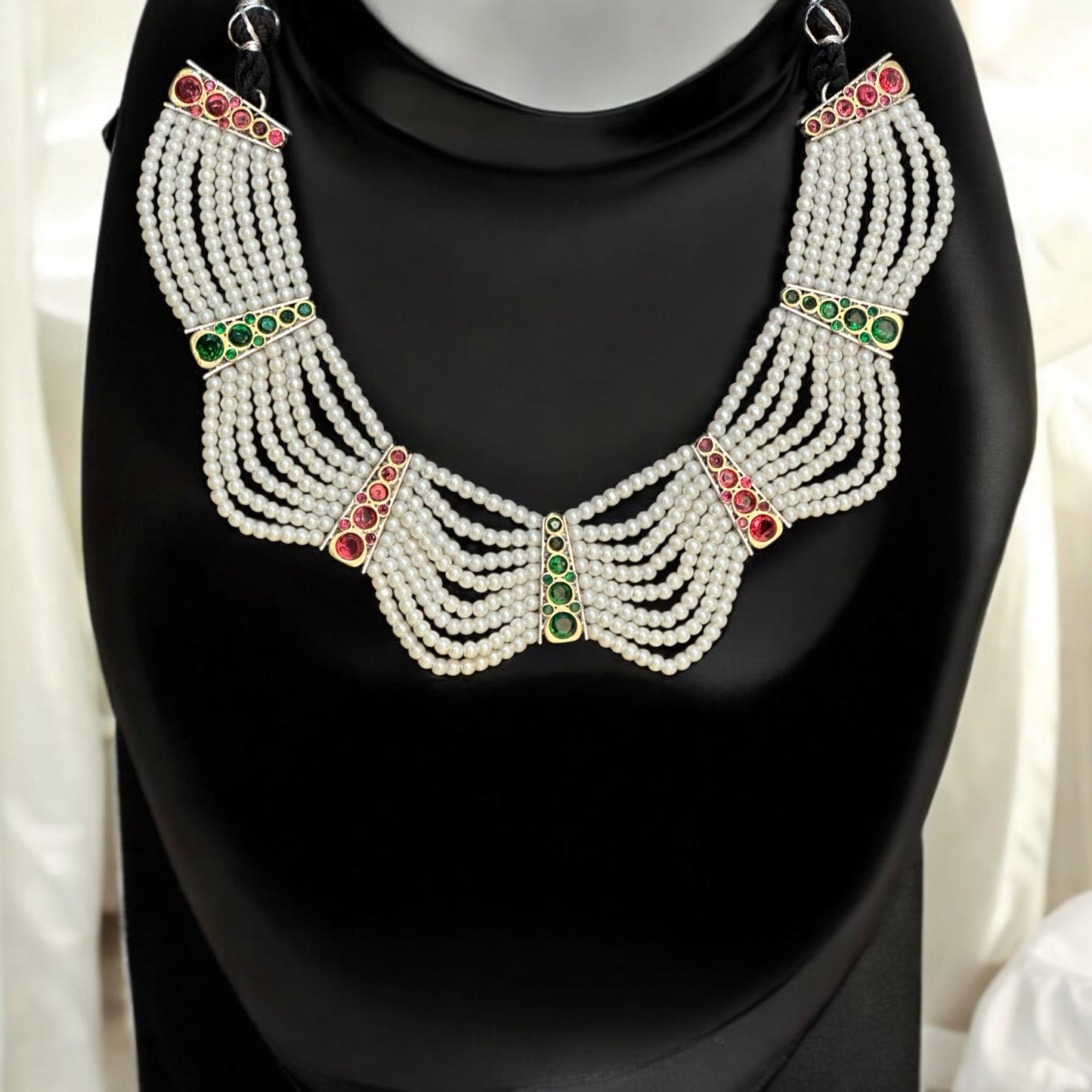 Elegant pearl necklace with red and green stone accents, perfect for festive and traditional occasions placed on a black jewellery display stand.