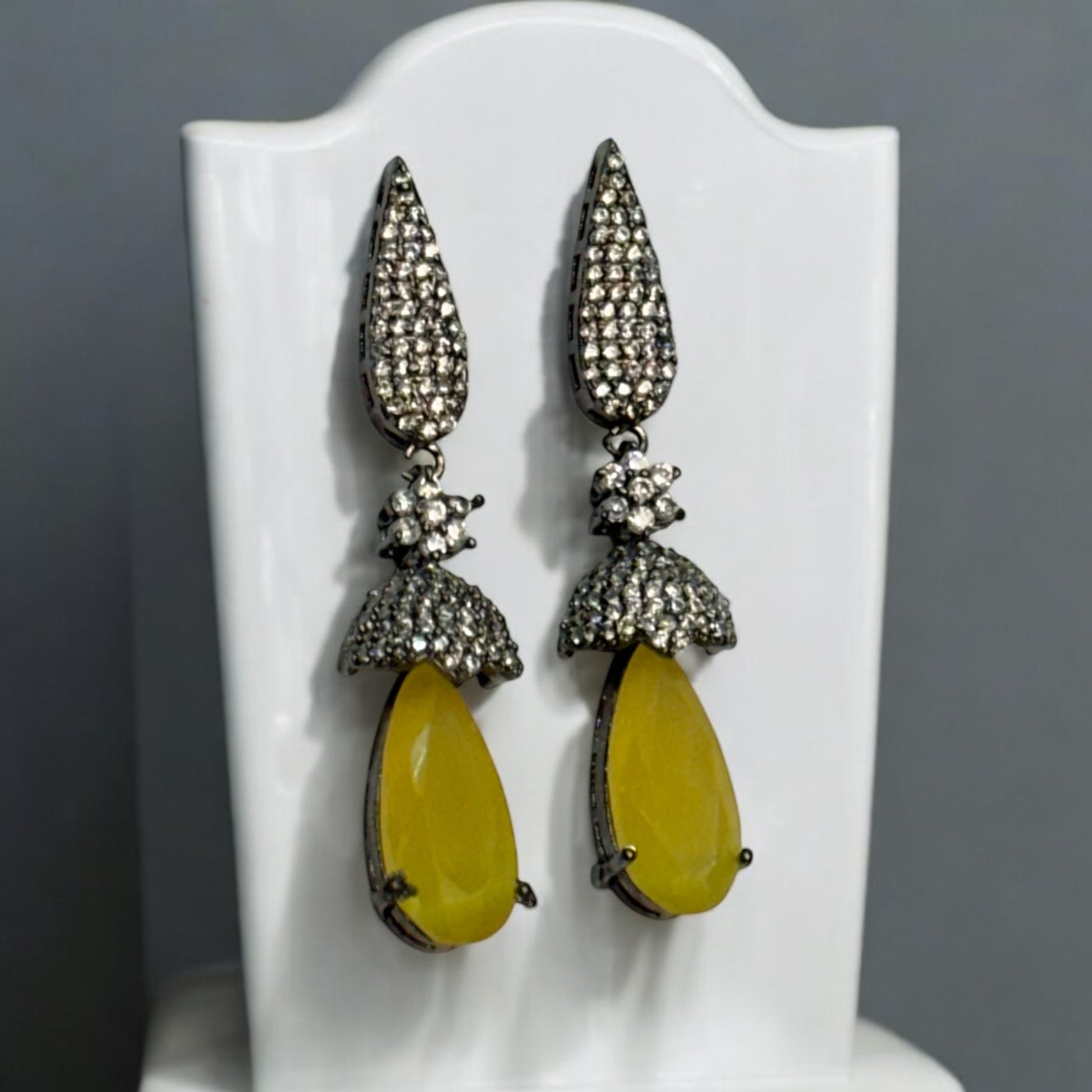 Elegant American diamond statement earrings featuring yellow drop stones and intricate black-polished detailing displayed on a white jewellery display stand.