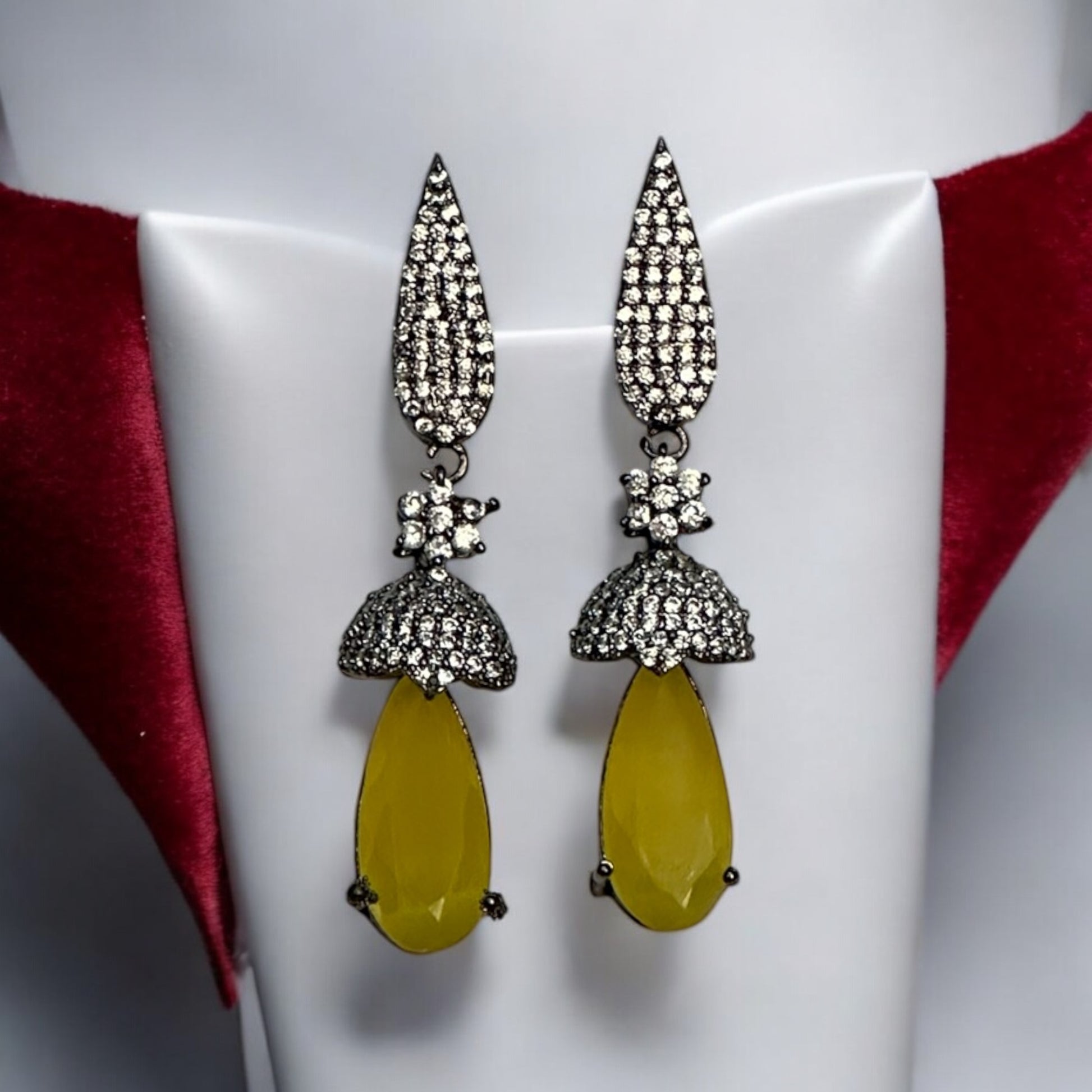 Elegant American diamond statement earrings featuring yellow drop stones and intricate black-polished detailing displayed on a red white jewellery display stand.