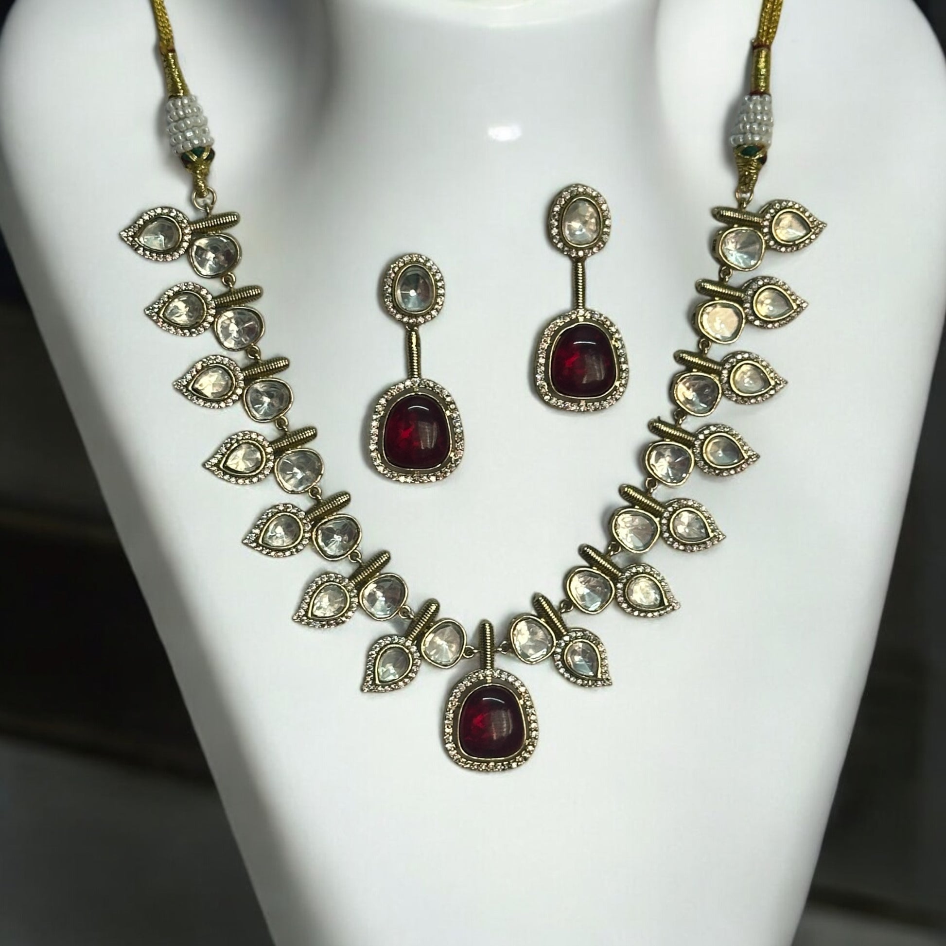 Elegant designer polki kundan necklace with teardrop accents and red gemstone centerpiece, paired with matching earrings.