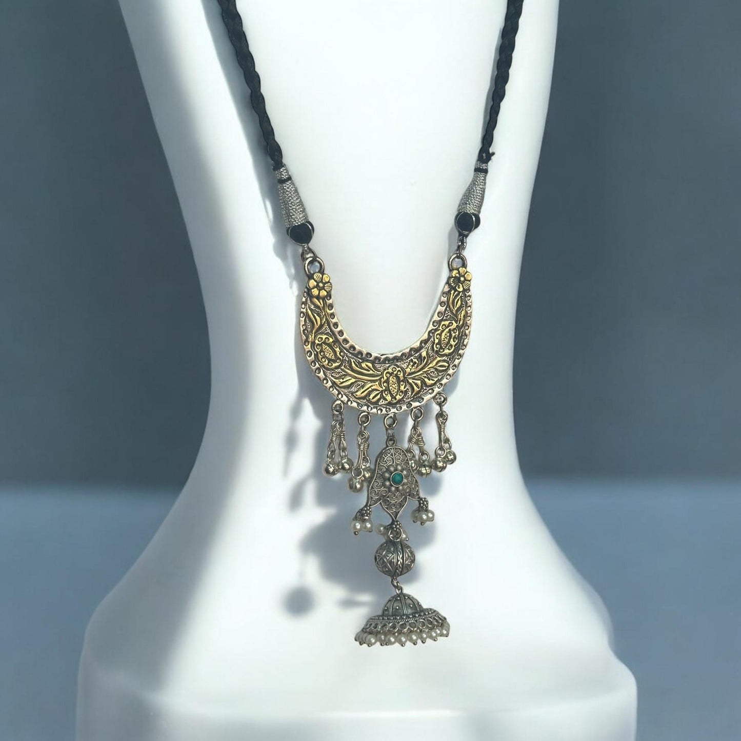 Side view of Fusion Handmade Necklace with a gold-toned crescent pendant featuring detailed engravings, oxidized silver charms, turquoise stone, and jhumka drop, displayed on a white mannequin background.