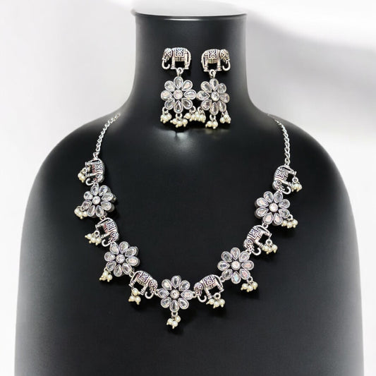 German silver necklace set featuring intricate elephant motifs and floral pendants adorned with dangling pearls, paired with matching earrings. Displayed on a black mannequin bust against a plain background.