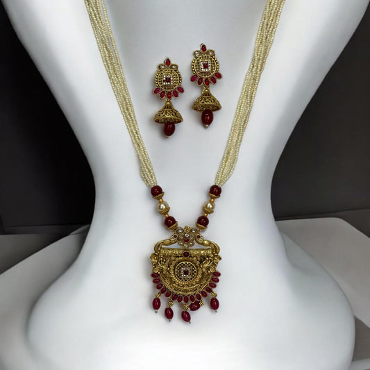 Traditional gold-toned long necklace set featuring a detailed pendant with red stones and pearl bead chains, paired with matching dangler earrings, displayed on a white mannequin background.