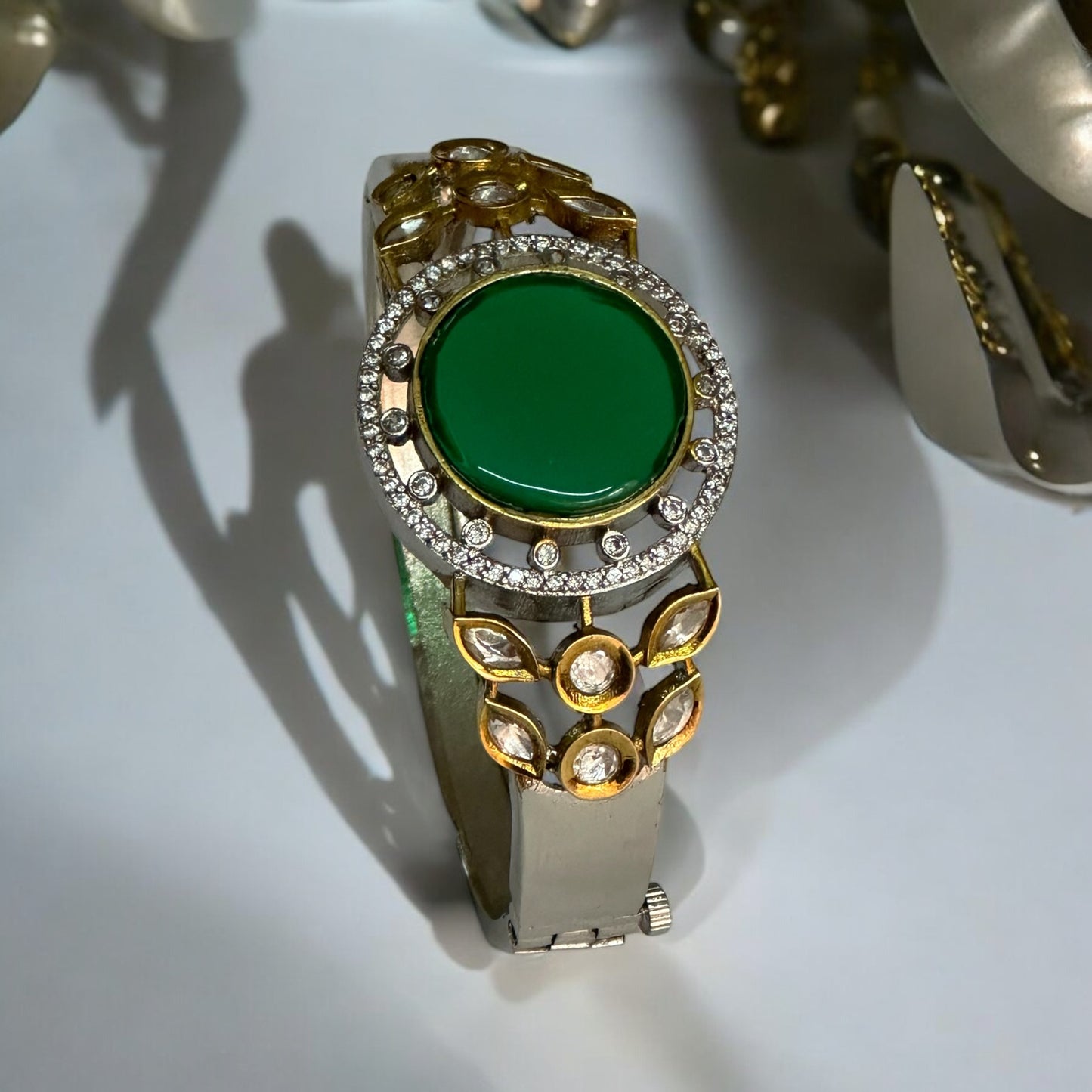 Top View of an Elegant Moissanite Bracelet featuring a vivid green Monalisa stone centerpiece with intricate gold and silver accents. It is placed on a white jewellery display stand.