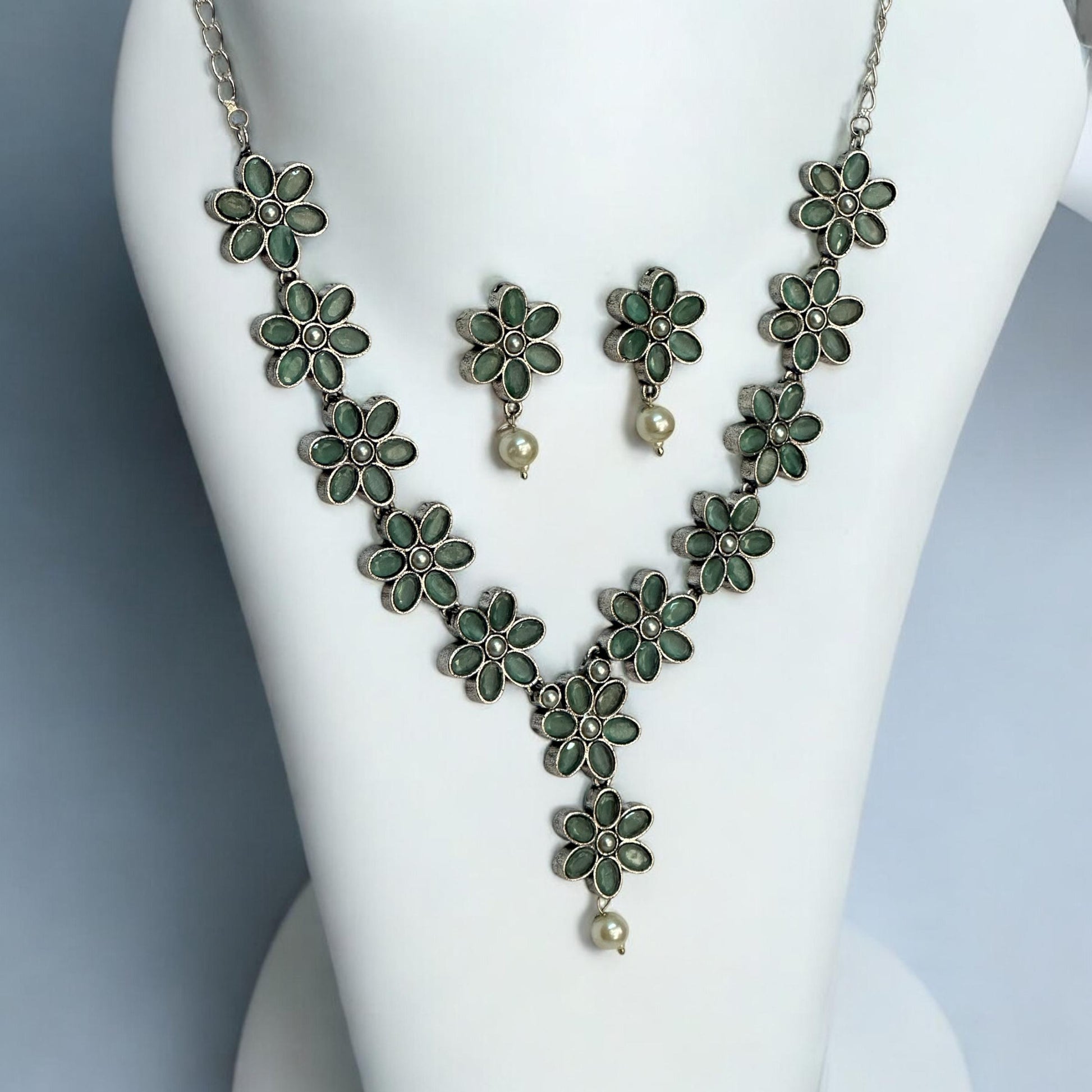 side view of Oxidised necklace set with mint green flower-shaped motifs and pearl drops, paired with matching earrings, displayed on a white mannequin against a soft gray background.