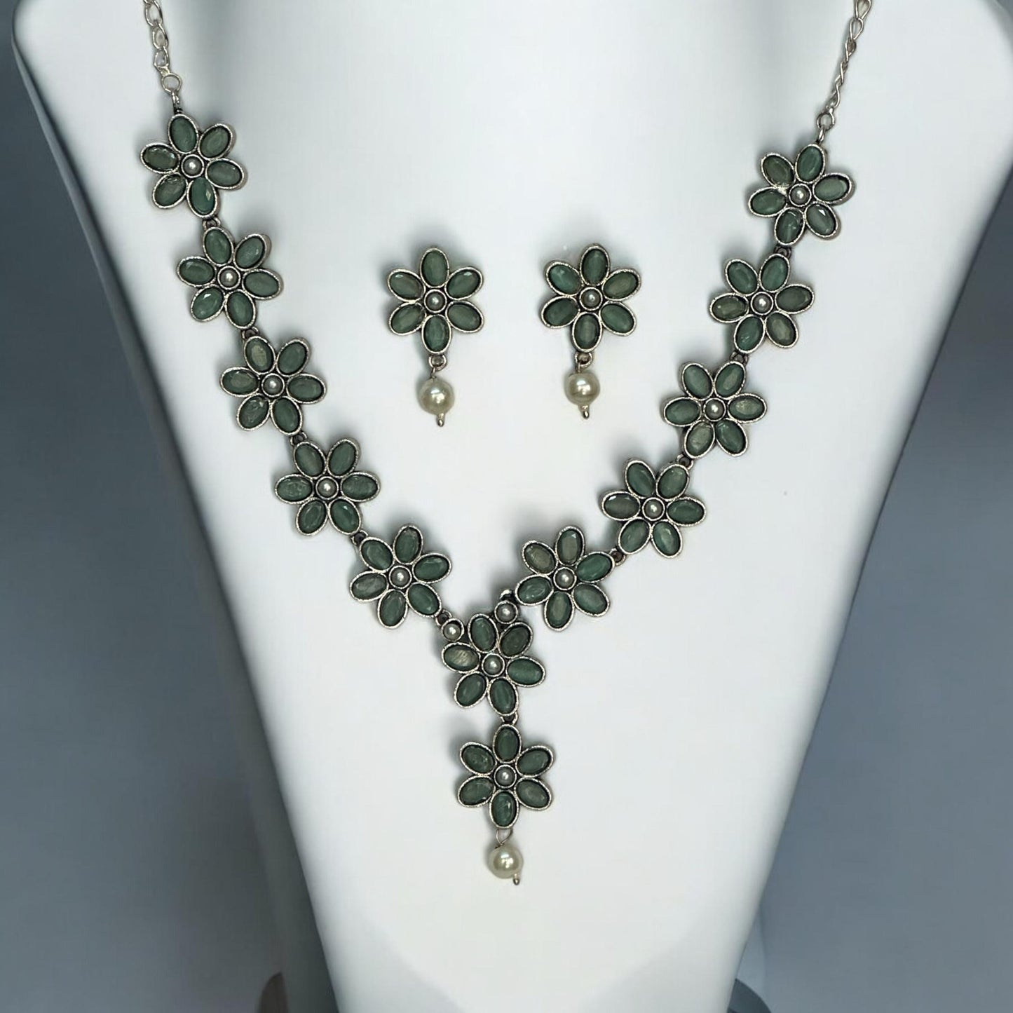 Oxidised necklace set with mint green flower-shaped motifs and pearl drops, paired with matching earrings, displayed on a white mannequin against a soft gray background.