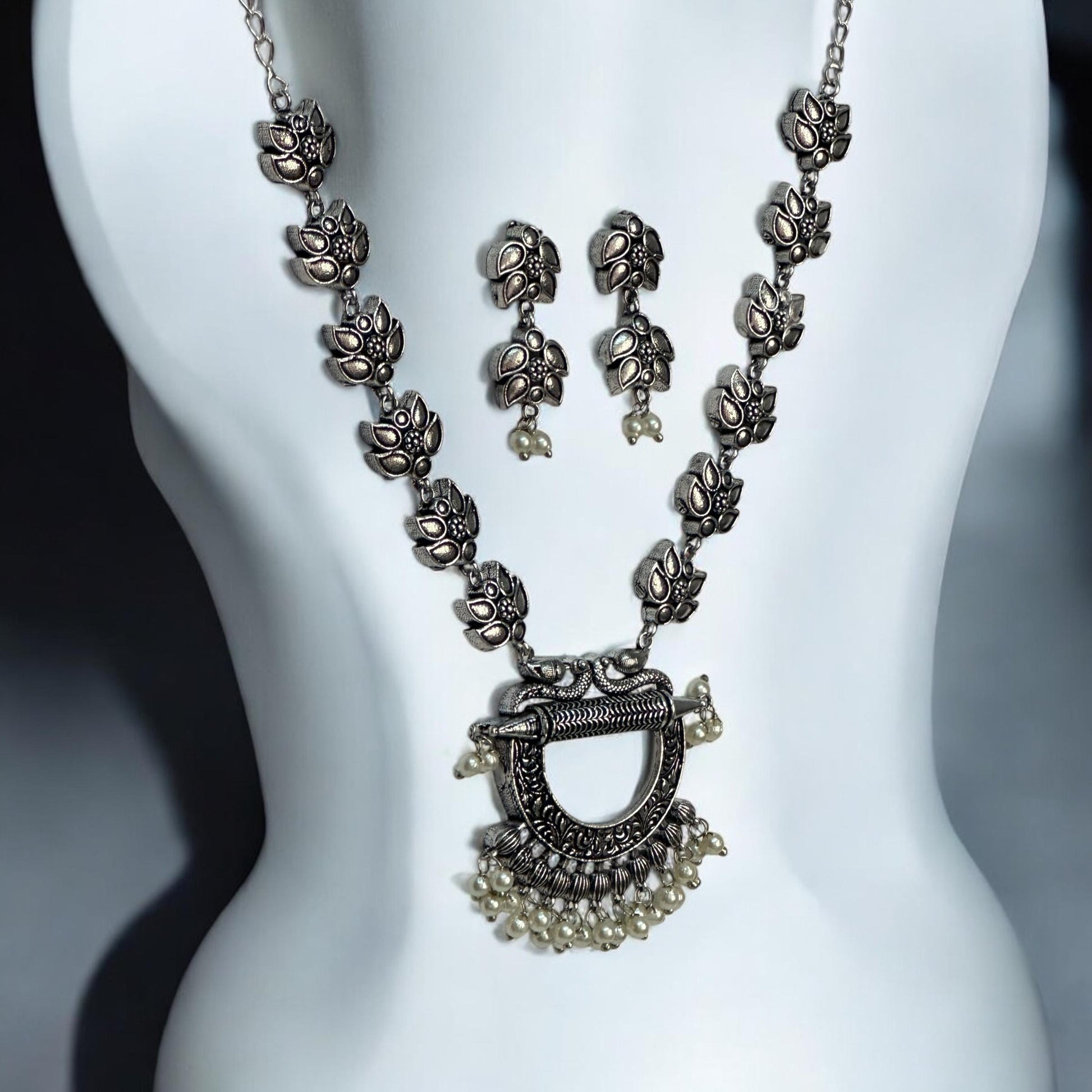 Oxidised necklace set featuring traditional motifs and pearl embellishments, displayed on a white mannequin with matching earrings against a soft gray background.