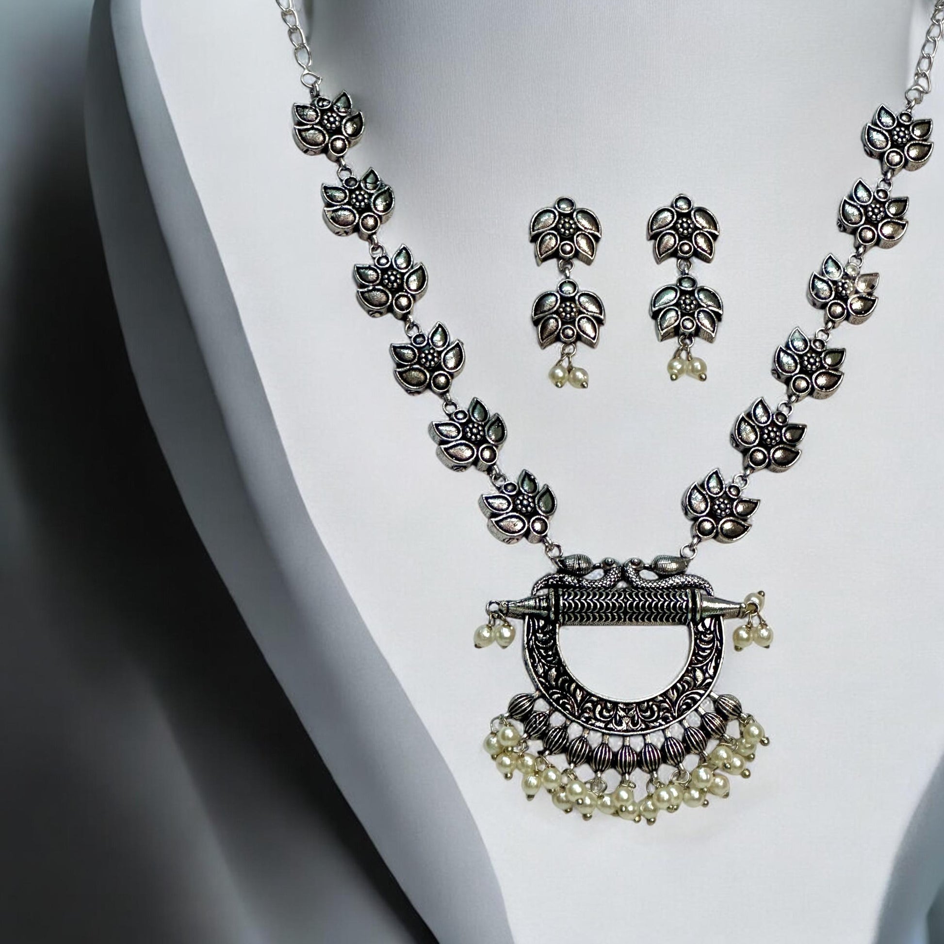 Side view of Oxidised necklace set featuring traditional motifs and pearl embellishments, displayed on a white mannequin with matching earrings against a soft gray background.