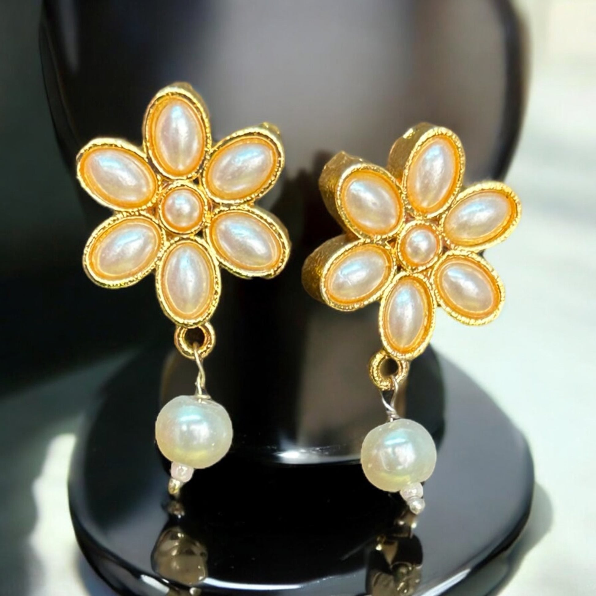 Gold-tone flower design earrings adorned with pearls, elegantly displayed on a black bust, perfect for adding grace to your outfit.