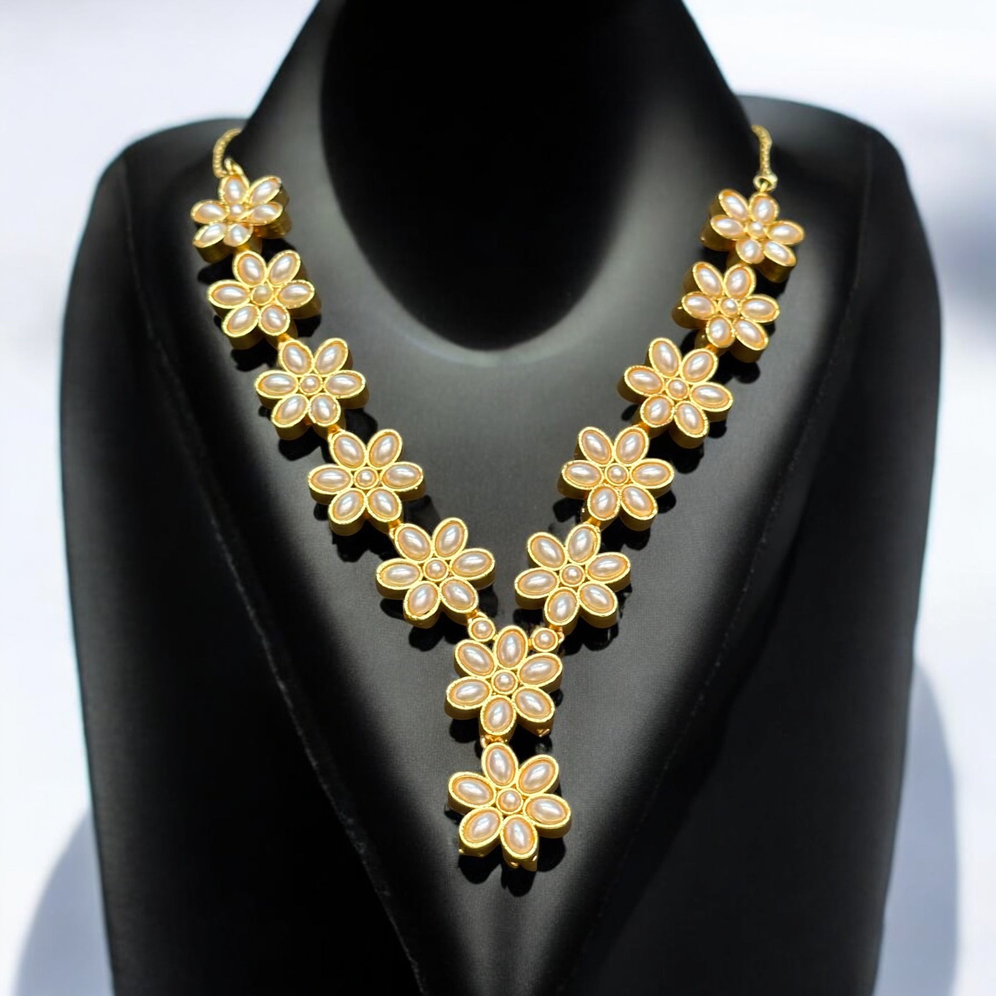 Gold-tone flower design necklace adorned with pearls, elegantly displayed on a black bust. Matching floral earrings with pearl drops complete the set, perfect for adding grace to your outfit. It is placed on a black coloured jewellery display stand.