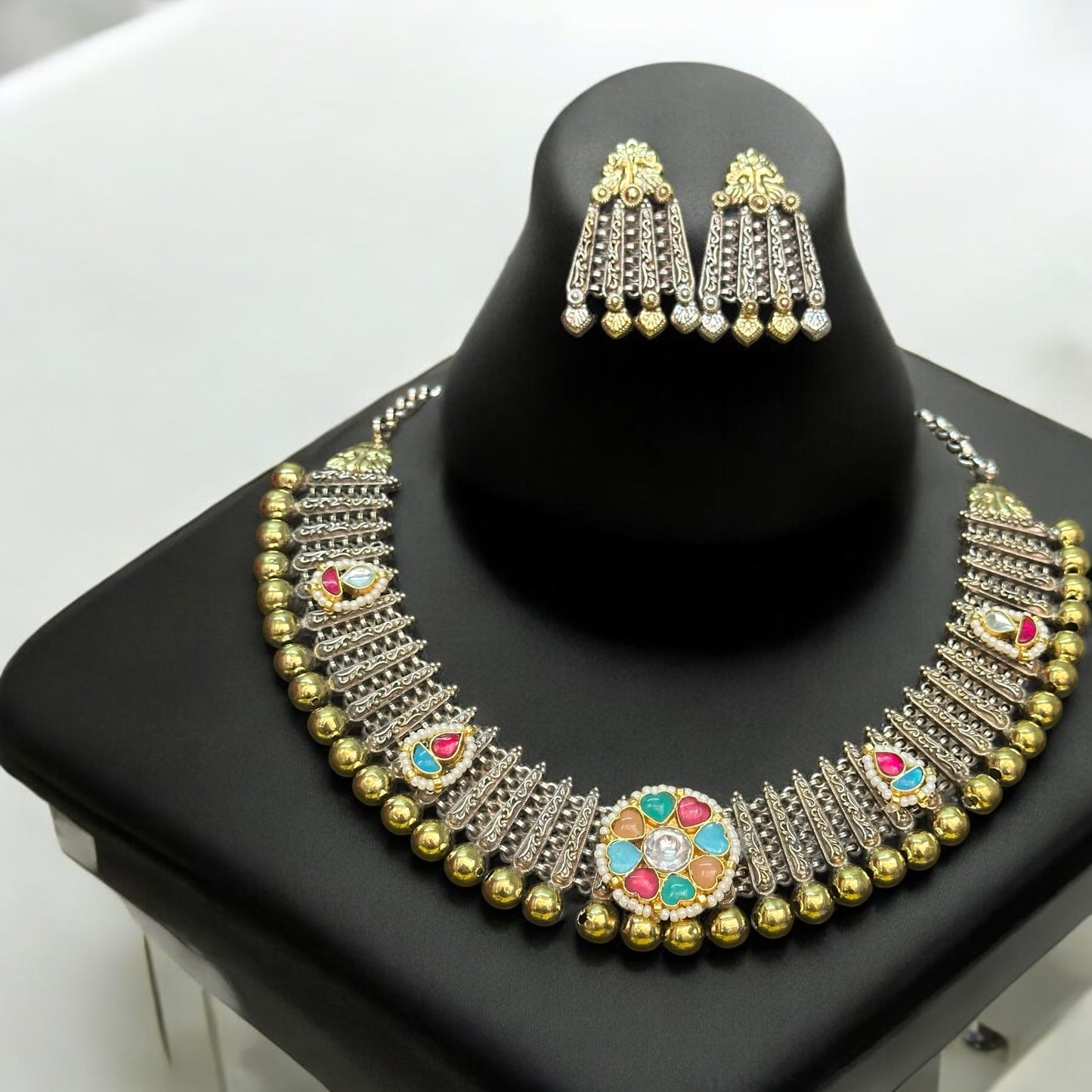 Premium silver replica kundan pachi necklace set featuring colorful stone detailing and traditional design, paired with matching chandelier earrings, displayed on a black bust stand.