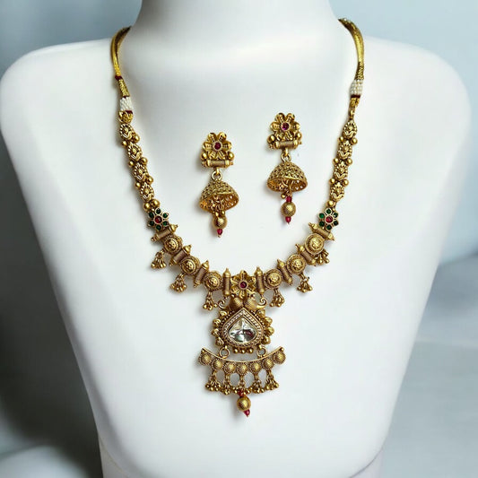 A Premium gold-plated kundan rajwadi necklace with a jhumki style earrings are placed on a white coloured jewellery display stand. 