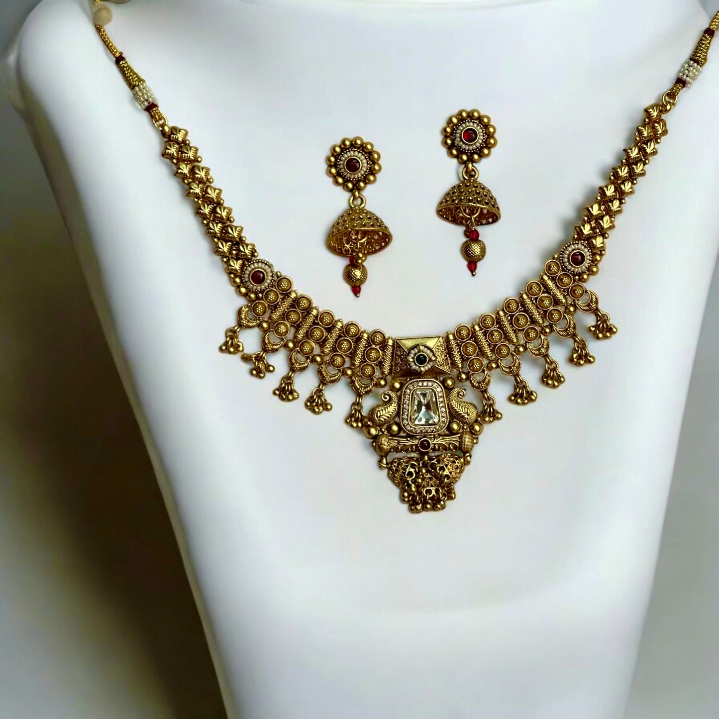 Exquisite Kundan Premium Rajwadi Necklace with intricate gold detailing and matching jhumka earrings, featuring regal red accents. Necklace set is placed on a white jewellery display stand.