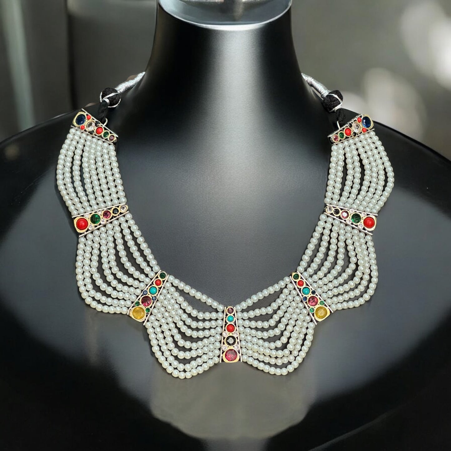 Royal Pearl Necklace featuring cascading pearl strands adorned with colorful gemstones in red, green, and yellow, displayed on a black mannequin with a neutral background.