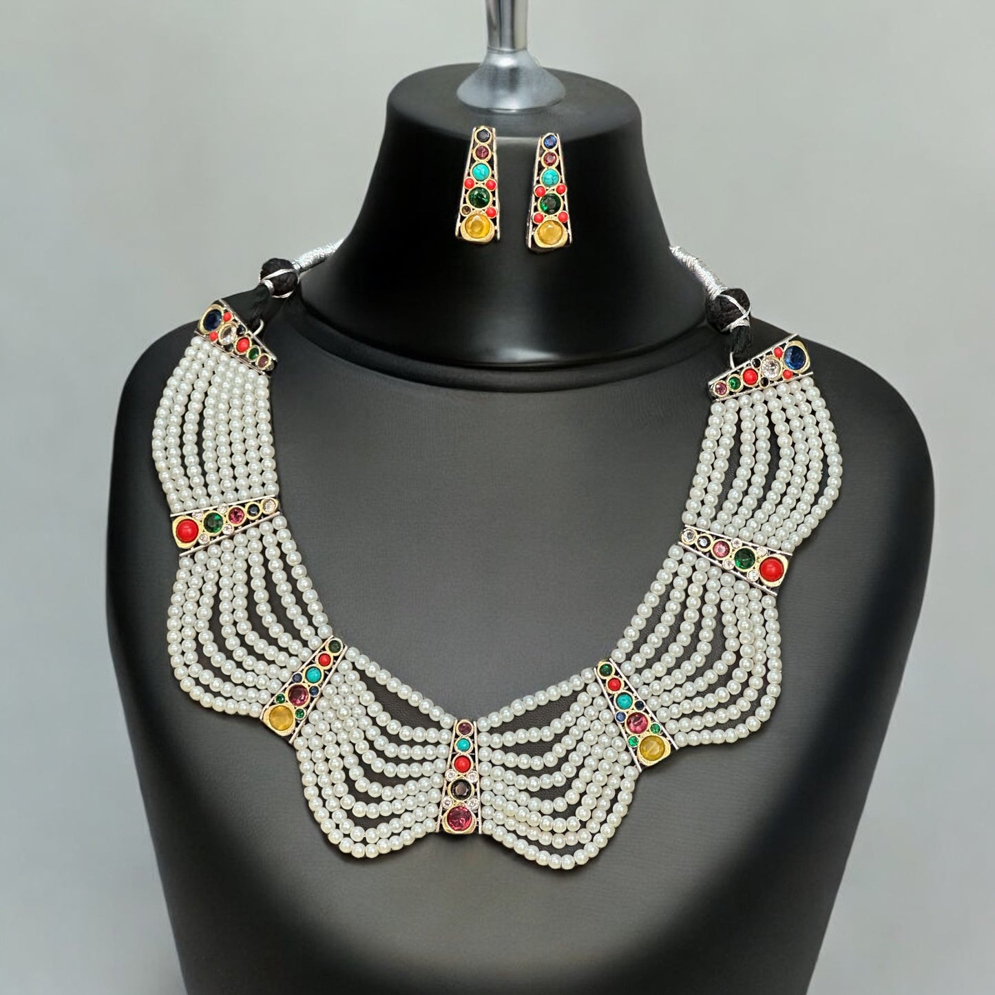 Royal Pearl Necklace featuring cascading pearl strands adorned with colorful gemstones in red, green, and yellow, paired with matching stud earrings, displayed on a black mannequin with a neutral background.