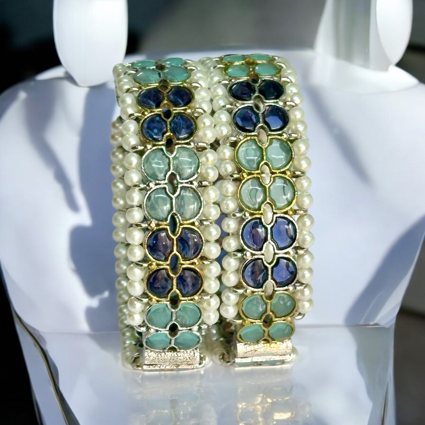 Silver replica bangles with intricate green and blue enamel accents and pearl detailing. Placed on a white colored jewellery display stand.