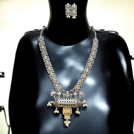 Silver Replica Necklace Set with intricate detailing and yellow accents, paired with matching stud earrings, displayed on a black mannequin, featuring a statement cylindrical pendant with pearl and gold embellishments.