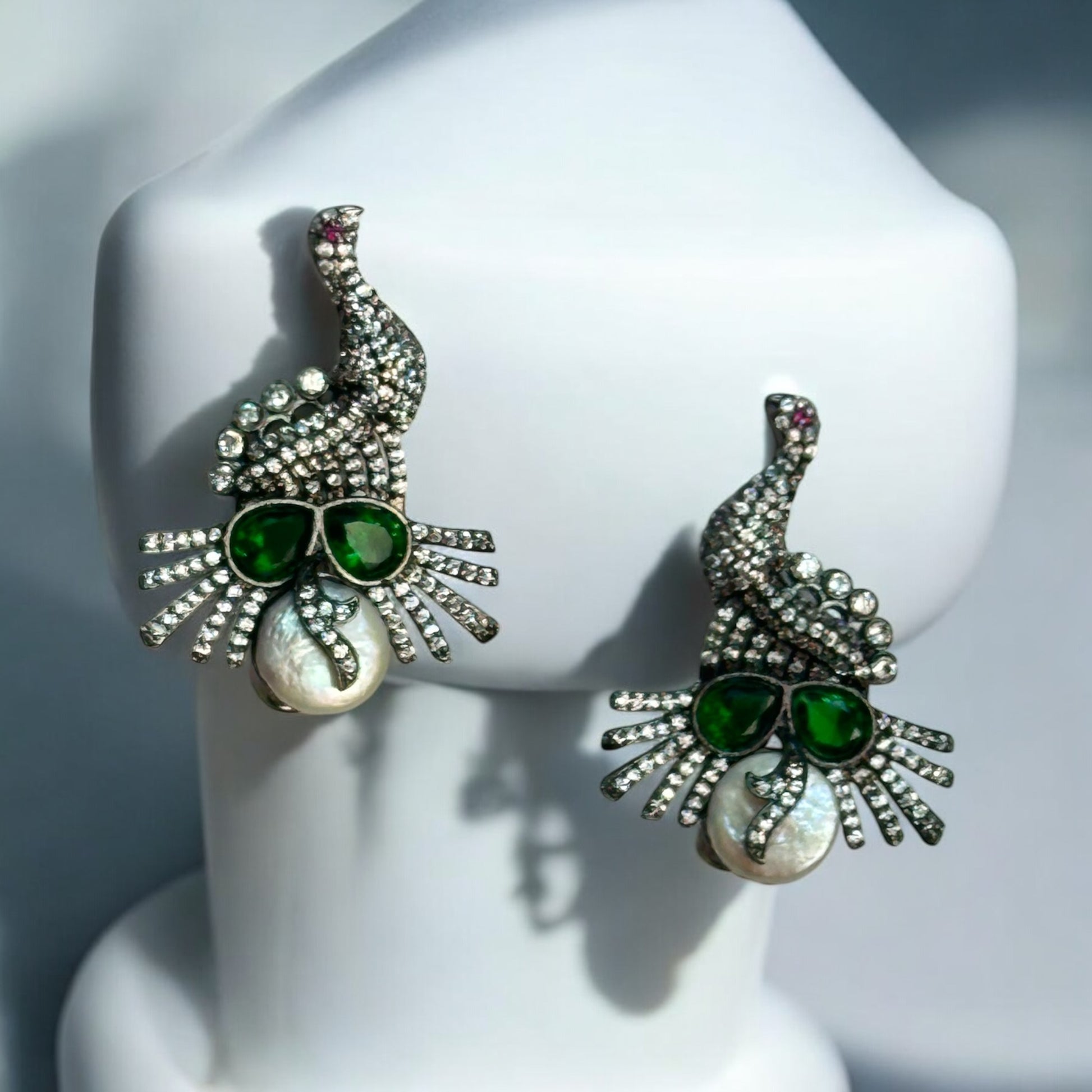 American Diamond Party Wear Earrings placed on a white jewellery display stand having – peacock-inspired earrings with green stones, white pearls, and a double-lock mechanism. A stunning choice for festive and formal occasions.