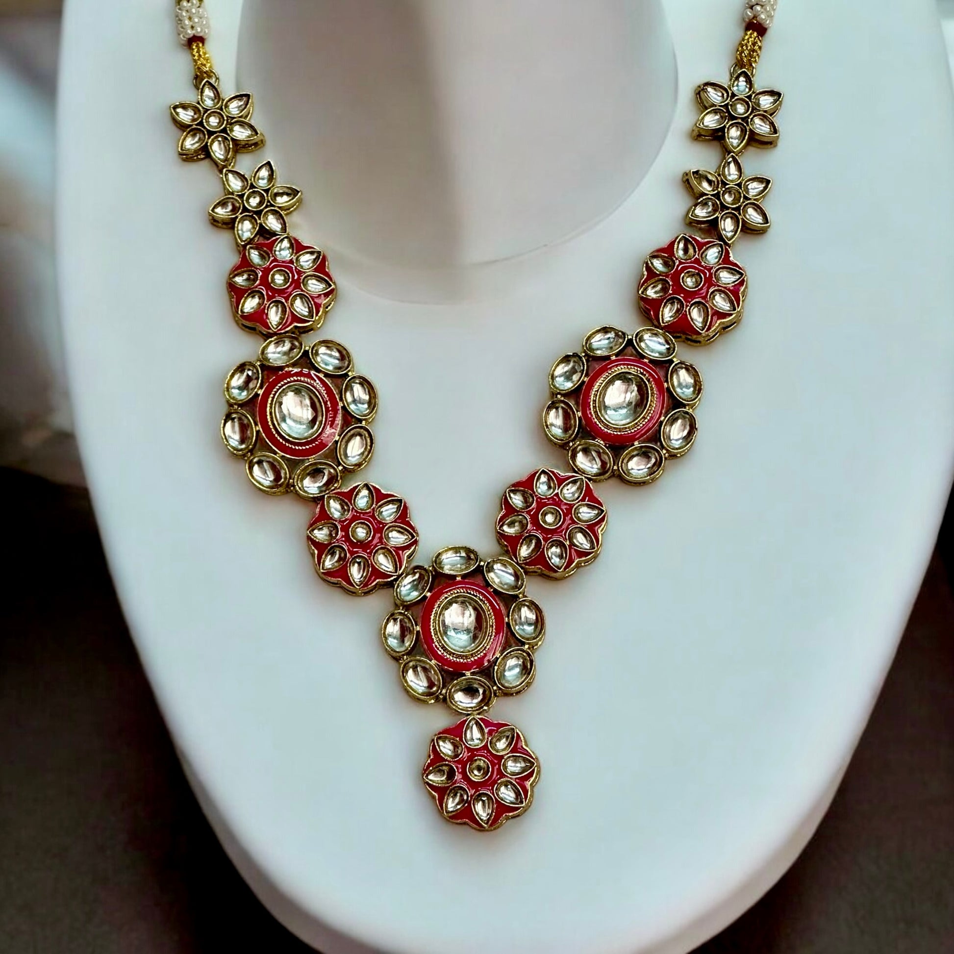 Elegant Kundan necklace featuring intricate floral designs in pink and gold tones, placed on a white coloured jewellery display stand. These are perfect for traditional and festive occasions.