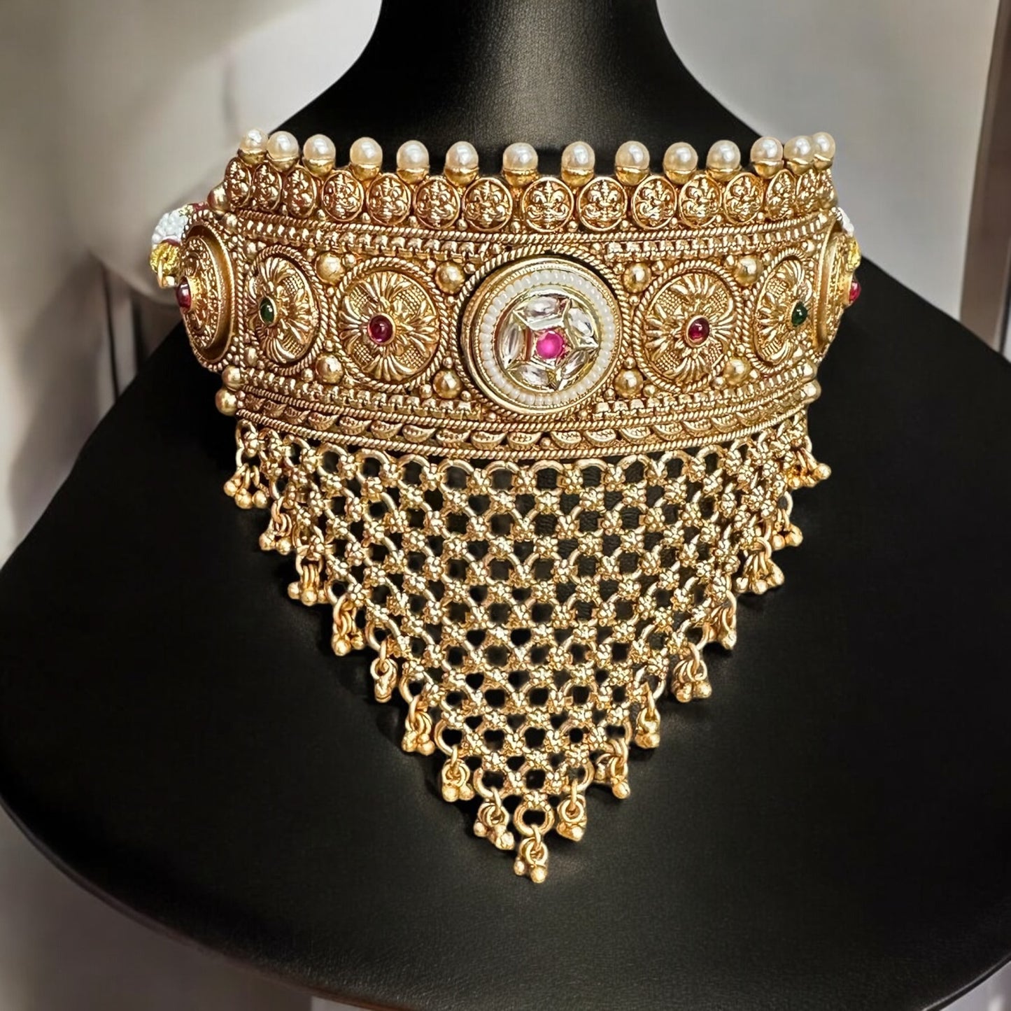 Rajawadi Kundan Choker Necklace in gold-tone choker with intricate kundan work, pearls, cascading mesh detailing placed on a black jewellery display stand. Ideal for weddings and festive occasions.