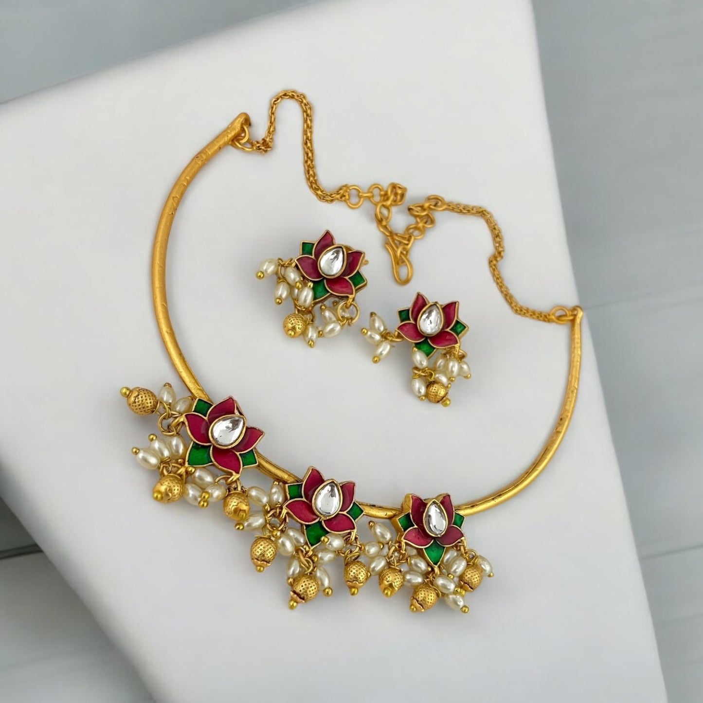 Temple Necklace in Hasli Lotus Design – gold-tone necklace featuring red and green enamel lotus motifs, polki stones, pearl drops, and matching earrings. Ideal for weddings and festive occasions.